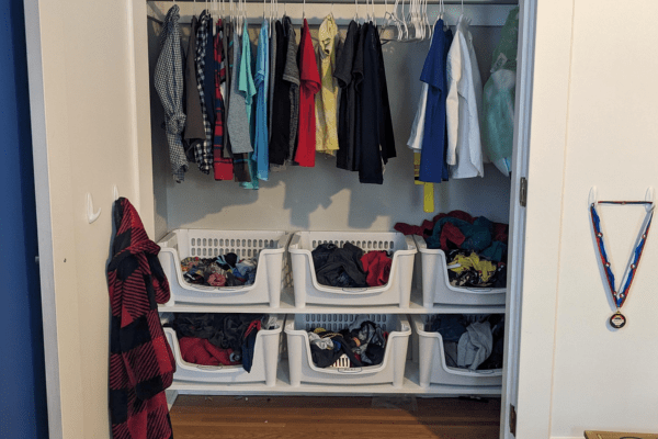 A kids' closet with clothes hanging and open bins