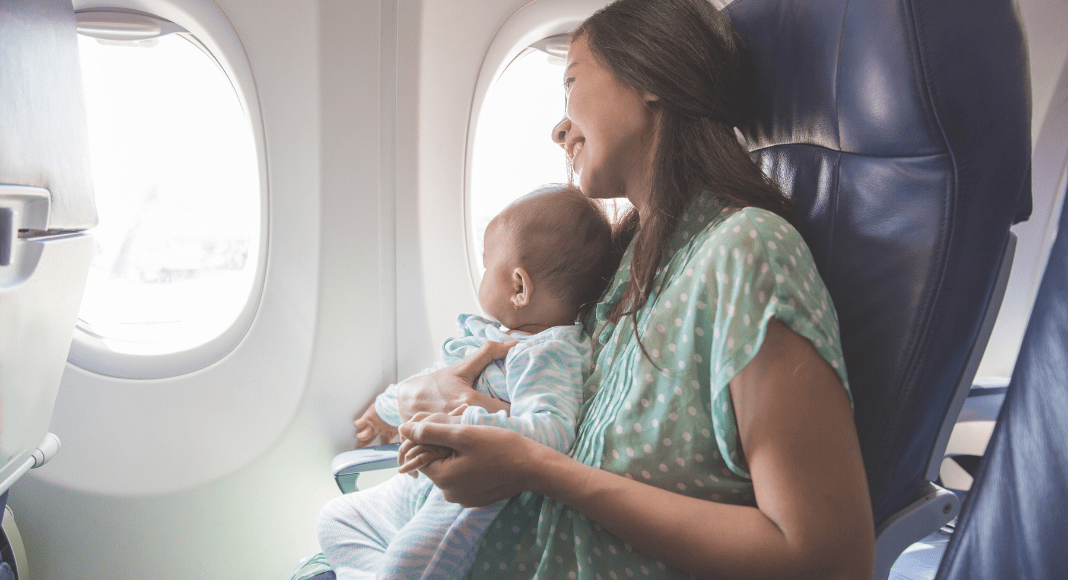 A mom and baby look out the window on an airplane.