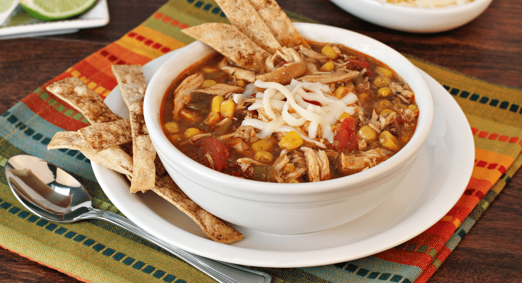A delicious bowl of soup with chicken beans, corn and tortilla strips sits on a table.