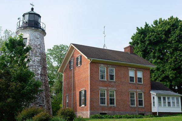 A lighthouse stands next to a red brick house.