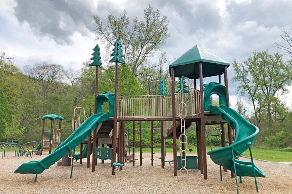 A woody playground with green slides and pine trees.