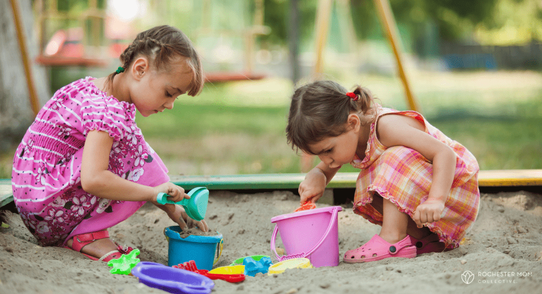 Two girls play in a sandbox at a playground.