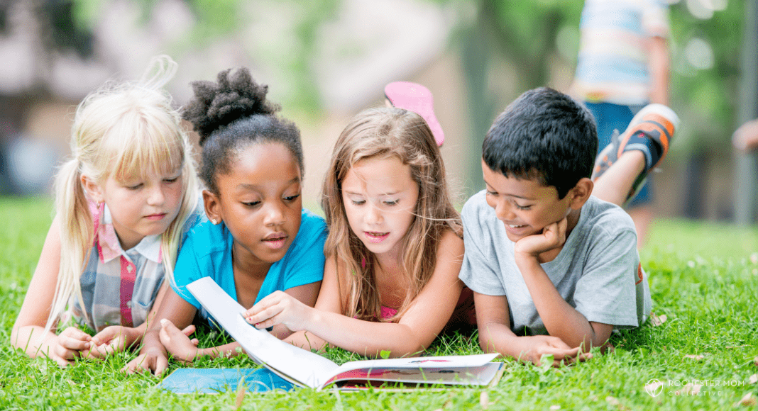 Kids sit outside on the grass looking at a book together.