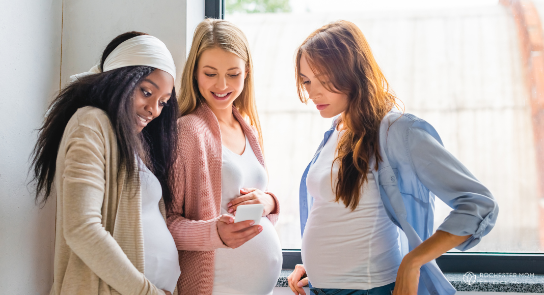 Three pregnant women look at information on a cell phone together.